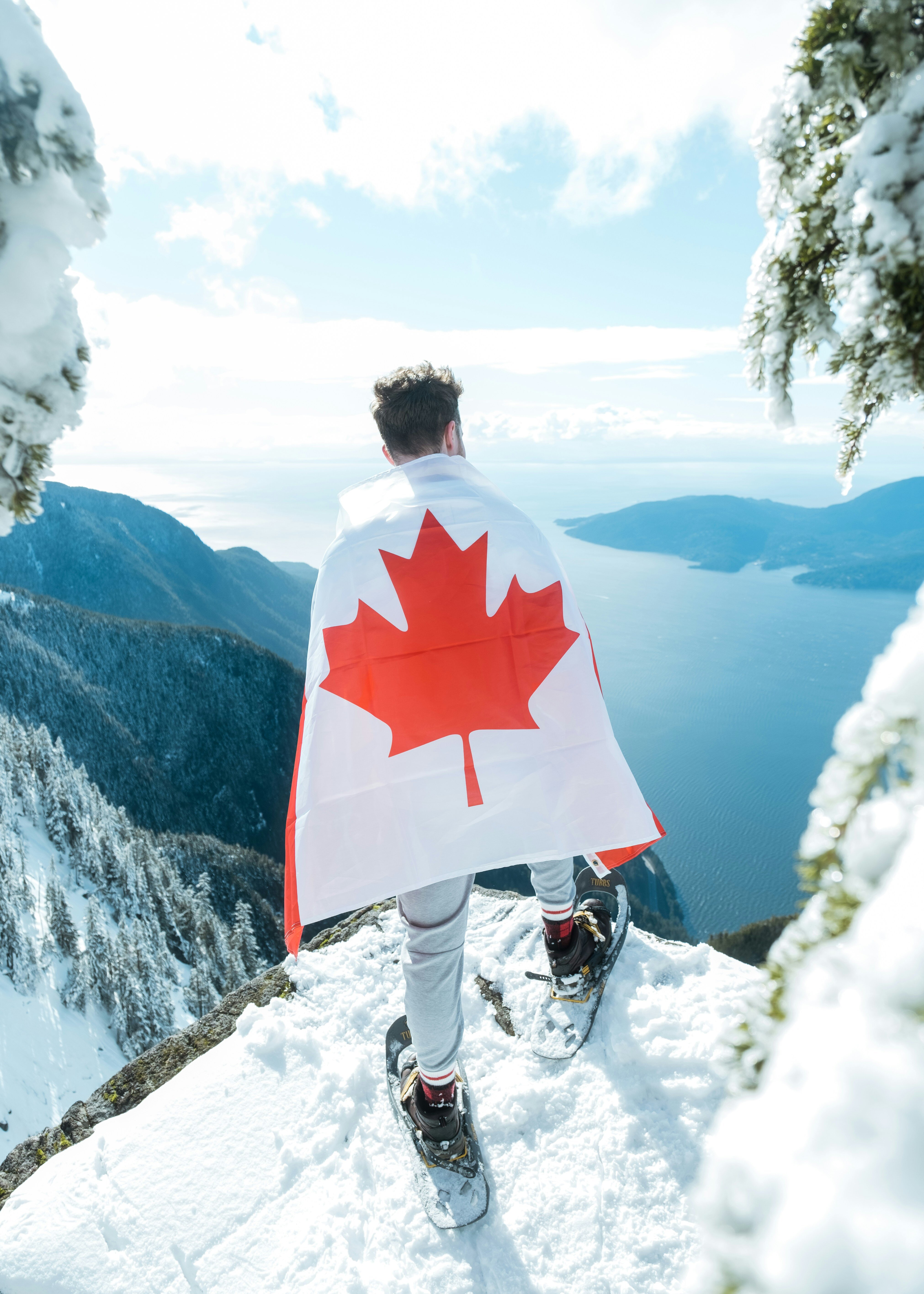 guy wrspped in a acanadian flag standing on a snowy mountain